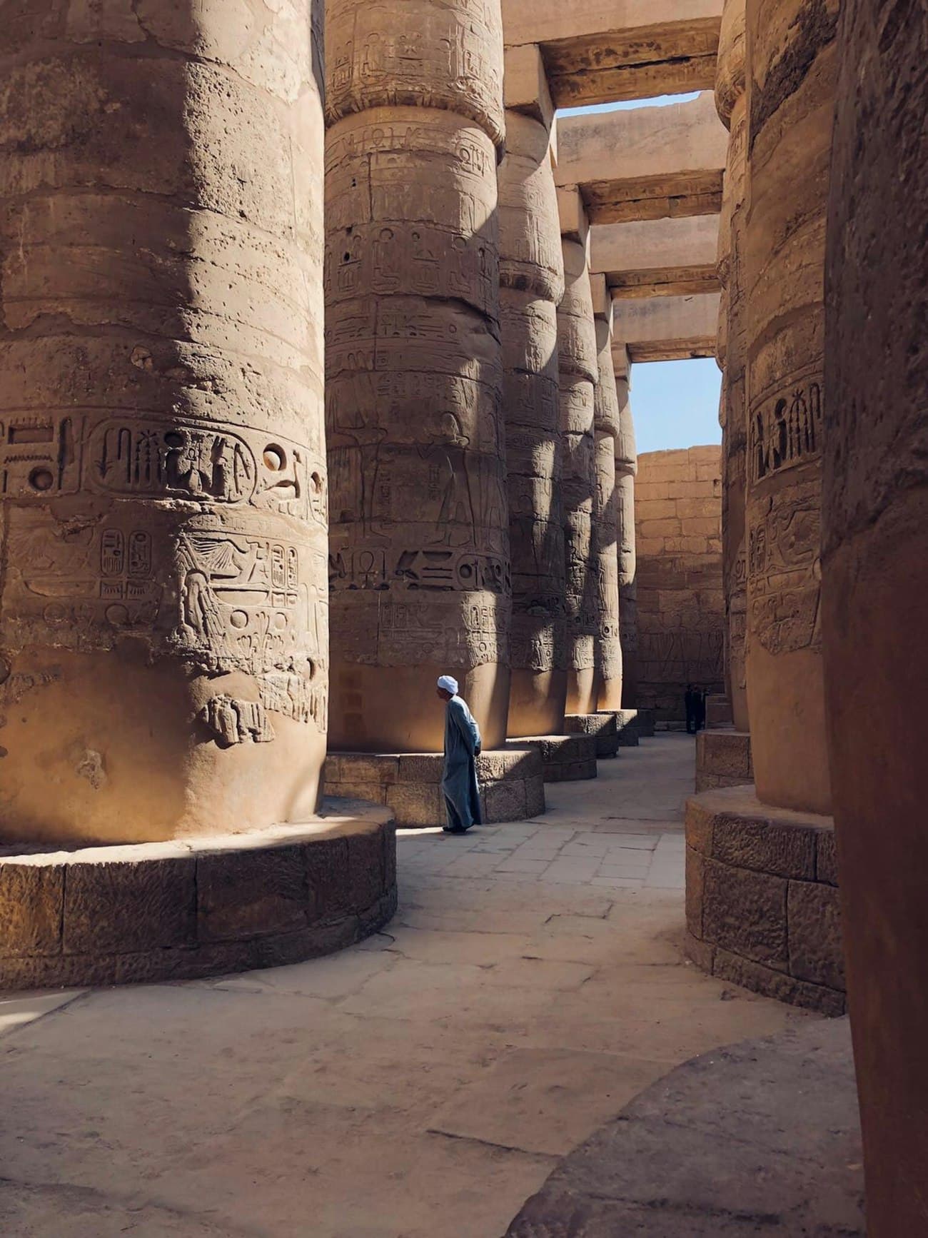 A visitor standing among the carved columns of a temple hall in Luxor